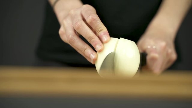 Las manos de una chica joven trocean una cebolla sobre una tabla de madera.