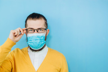 A young man in a medical mask on a blue background. A man in a yellow cardigan shows a hand gesture OK. We're going to beat coronavirus. The COVID-2019 epidemic. Positive boy.