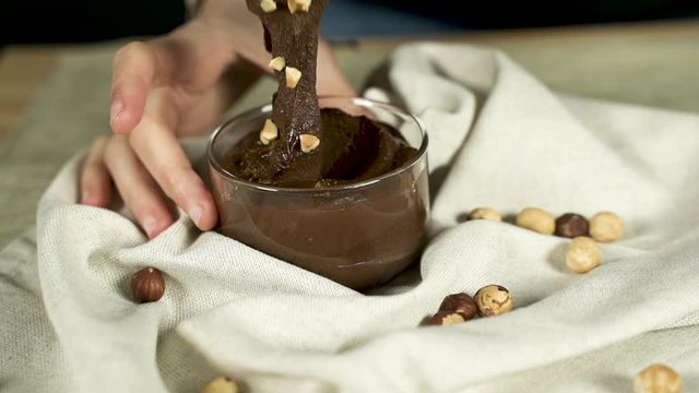 Manos de una mujer cogen una porci&oacute;n de crema de cacao y avellanas. 