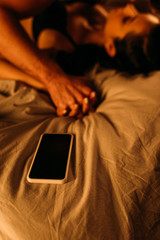 Selective focus of couple with clenched hands lying near smartphone on bed in bedroom