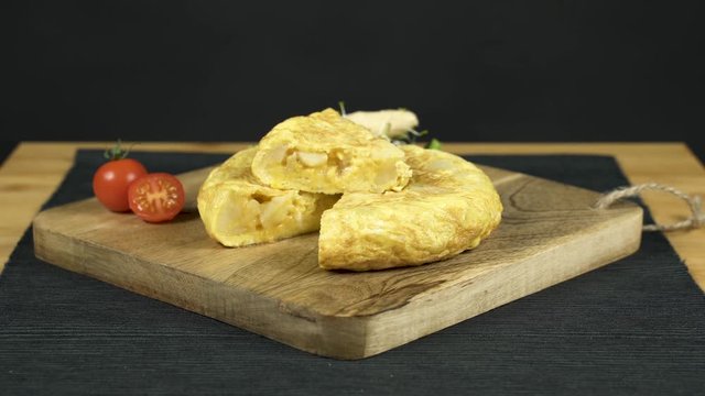 Tortilla de patatas sobre una tabla de madera acompa&ntilde;ada de unos tomates troceados.