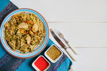 The national dish is Uzbek pilaf with chicken on the blue striped mat lying on a white background. There are also Cutlery and condiments nearby. Flat layout
