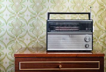 Antique radio on the nightstand in the room against the background of vintage wallpaper.