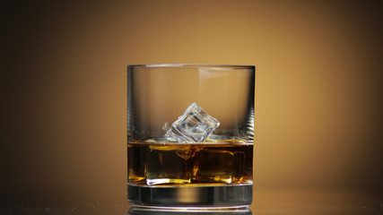 Alcohol drink whiskey, cognac into glass with ice cubes. Dark background.