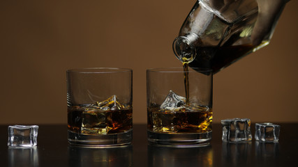 Pouring whiskey, cognac into glass. Brown background. Pour of alcohol drink
