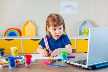 Little girl molding colorful rainbow from play clay watching online learning lesson