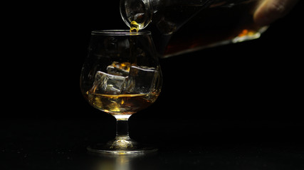 Pouring whiskey, cognac into glass. Black background. Pour of alcohol drink