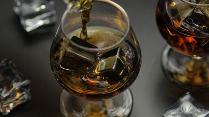 Pouring whiskey, cognac into glass. Black background. Pour of alcohol drink
