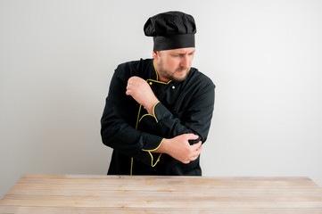 Fototapeta premium Young male chef in black uniform has elbow pain