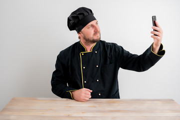 Young male chef in black uniform taking selfie photography