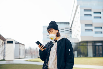 millenial girl in black minimal clothes using smartphone with respiratory mask on her face