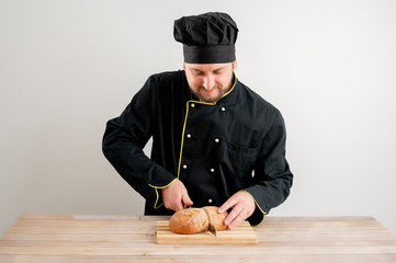 Young male chef in black uniform cut the bread with a knife