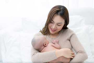 Asian mom tenderly cuddles the newborn baby while the infant is sleeping on the chest.
