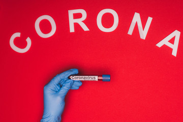 Top view of doctor holding test tube with blood sample and corona lettering on red background