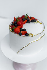 A beautiful white cake with cheese cream, meringues, chocolate and fresh Berries on a white background. The original idea for a wedding cake or birthday cake.
