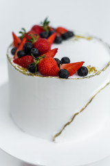 A beautiful white cake with cheese cream, meringues, chocolate and fresh Berries on a white background. The original idea for a wedding cake or birthday cake.