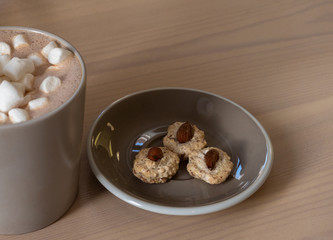 a dark Cup of coffee and marshmallows and a plate of cookies is placed on a wooden table. close up
