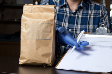 Paper bags with food. Nearby, a man in rubber gloves holds a delivery form and a pen in his hands. Home delivery during an epidemic.