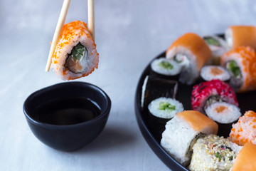 Sushi over the sauce is held by two chopsticks, next to a plate with sushi and rolls. sushi and roll delivery, contactless delivery during the coronavirus epidemic