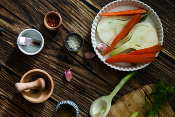 fennel, carrots and spices in a white ceramic pan on a wooden background top view