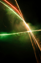 Abstract photography of orange, red and green fireworks in lines with smoke, black background