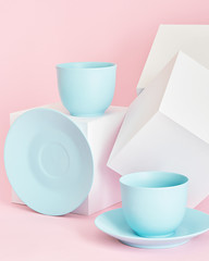 minimalism concept with light pastel colored blue cups and plate with white paper cubs on pink background.