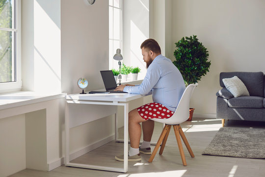 Online work at home. Funny fat businessman in red shorts works communicates using laptop at home.