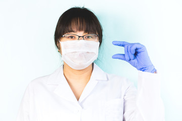 The woman wears a medical mask in a white uniform, protective blue, shows a small size of something. Selective focus