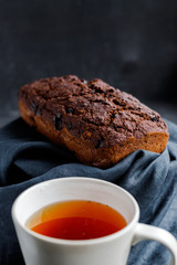 Freshly baked brownie cake on a linen napkin and black tea in a ceramic cup on a dark background. Daily homemade cakes. Cookbook advertisement. 