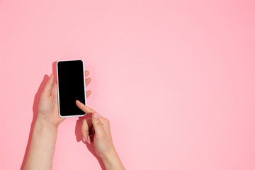 Hand using gadget, smartphone on top view, blank screen with copyspace, minimalistic style. Technologies, modern, marketing. Negative space for advertising. Coral color on background. Stylish, trendy.