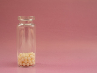 Homeopathic globules and glass bottle on pink background. Homeopathic Medicine