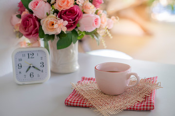 Cup of Black Coffee with vase of pink rose and white clock on a wooden desk,Working space at home.Urban Lifestyle concept.