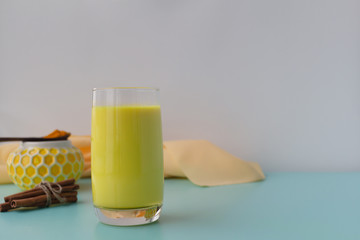 Golden milk in a glass cup with turmeric cinnamon and honey on a background. Useful drink for beauty and health with place for text.
