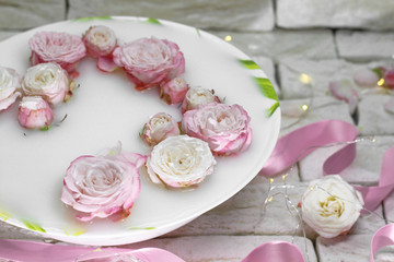 Dish with milk and small pink roses on a light background