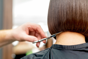 Back view of hairdresser hand is cutting hair tips of woman short hairstyle in hair salon.