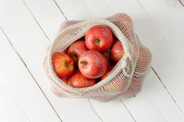 Apples in eco bag on white wooden background. Zero waste, eco friendly or plastic free lifestyle concept. 