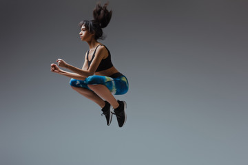 sportive african american girl in sportswear jumping on grey