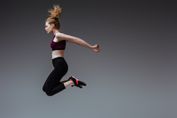 profile of curly woman in sportswear jumping on grey