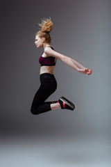 side view of curly woman in sportswear jumping on grey