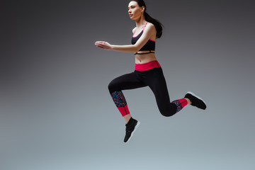 young and pretty woman in sportswear jumping on grey