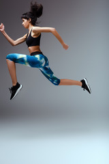 Obraz na płótnie Canvas side view of african american girl in sportswear jumping on grey