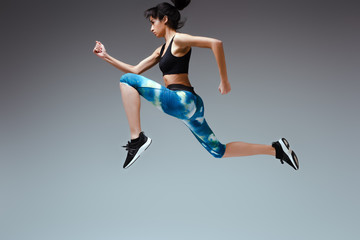 Fototapeta na wymiar side view of african american woman in sportswear jumping on grey