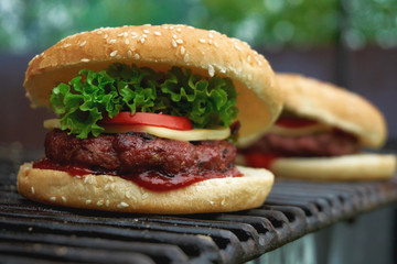 Close up of ready made tasty looking cheeseburger made of juicy grilled patty, cheese slice, fresh tomato and crispy lettuce leaf and ketchup added. Based on white bread bun with sesame seeds on top