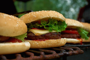 Prepared cheeseburgers standing on metal barbecue top in line ready to eat.Close up of fresh fast...