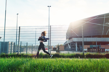 Young attractive female running on sunset in city with earphones listening to music during training