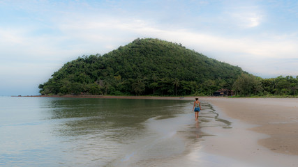 Thai woman in shorts and hat walking barefoot on beach at low tide