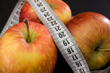 The concept of weight loss and diet. Three apples and a measuring tape on a black background....