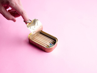 hand opening a tin with color pencils, isolated on pink background