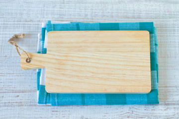 Empty  kitchen cutting board with handle and rustic towel on a wooden table, top view