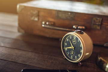 Vintage alarm clock on a wooden rustic table with travel case and strong backlight. Shallow DOF